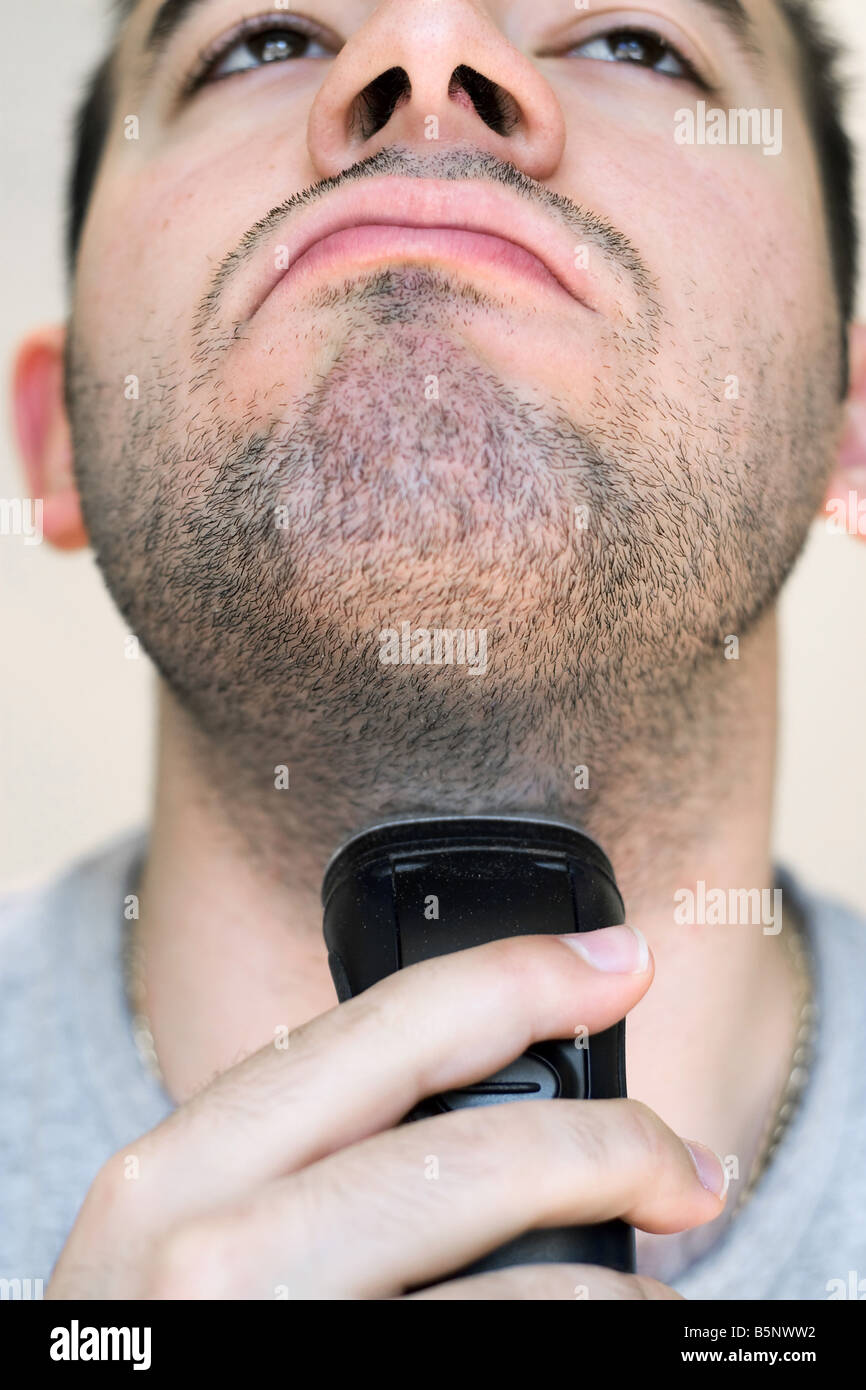 A closeup of a young man shaving his beard off with an electric shaver