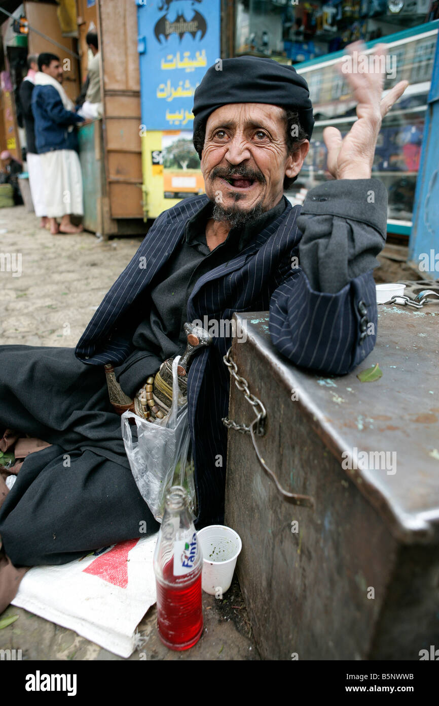 Old man sitting on pavement chewing Qat in the afternoon bag of Qat hanging from his Jambiya traditional dagger Yemen Stock Photo