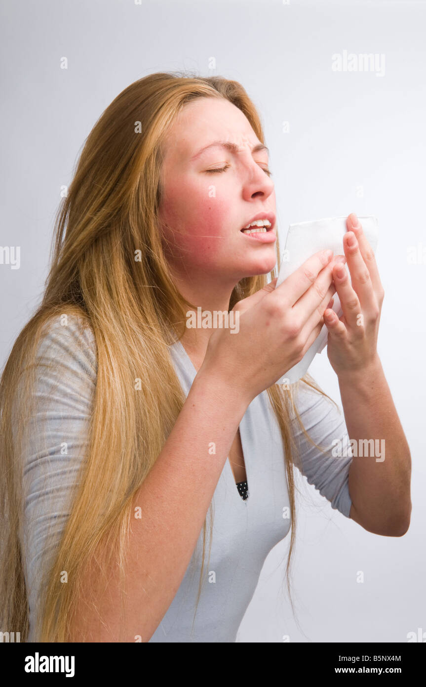 young blonde haired woman with a cold or flu about to sneeze into a paper handkerchief, UK Stock Photo