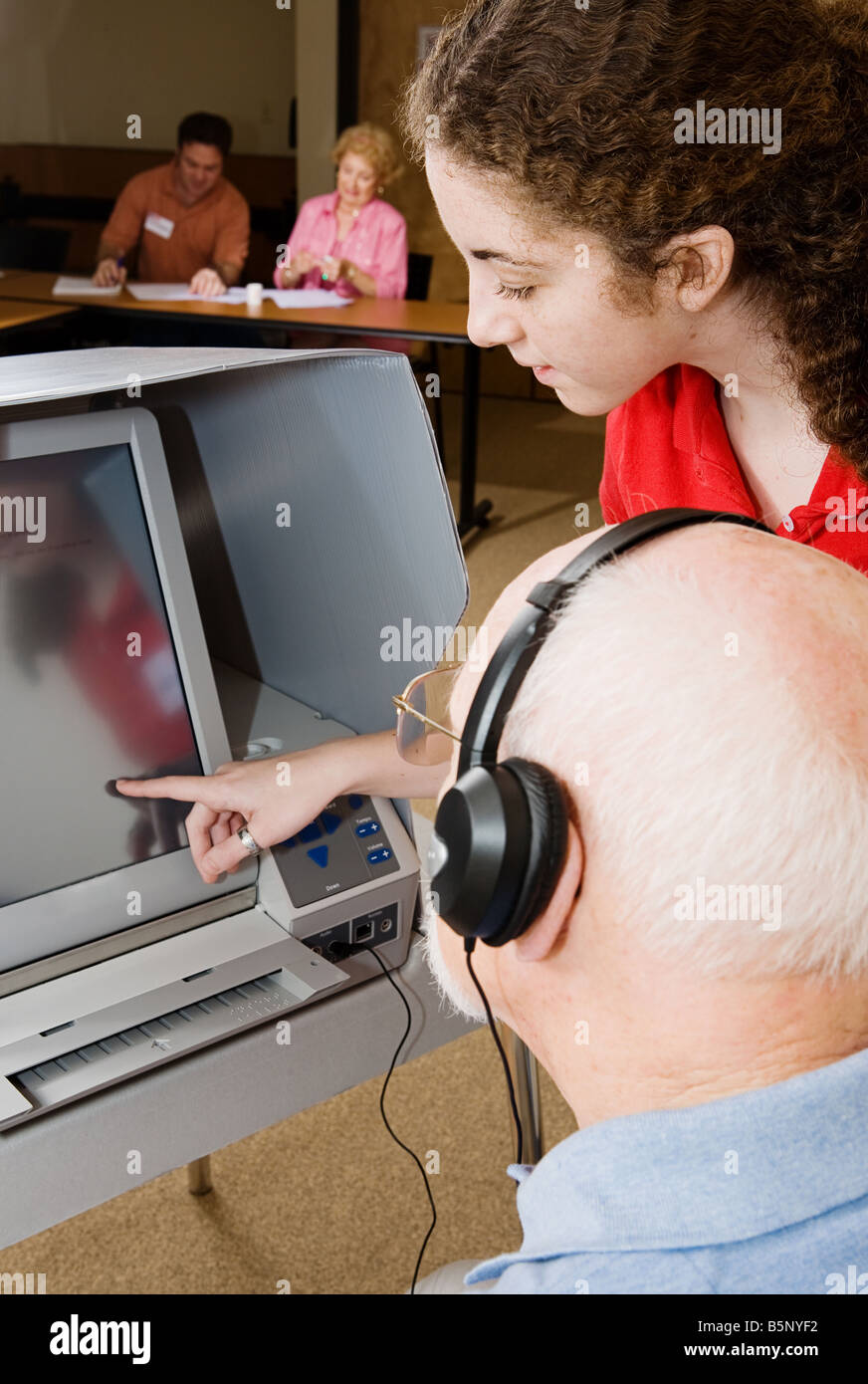 Teen poll worker assists senior voter on touch screen machine Stock Photo