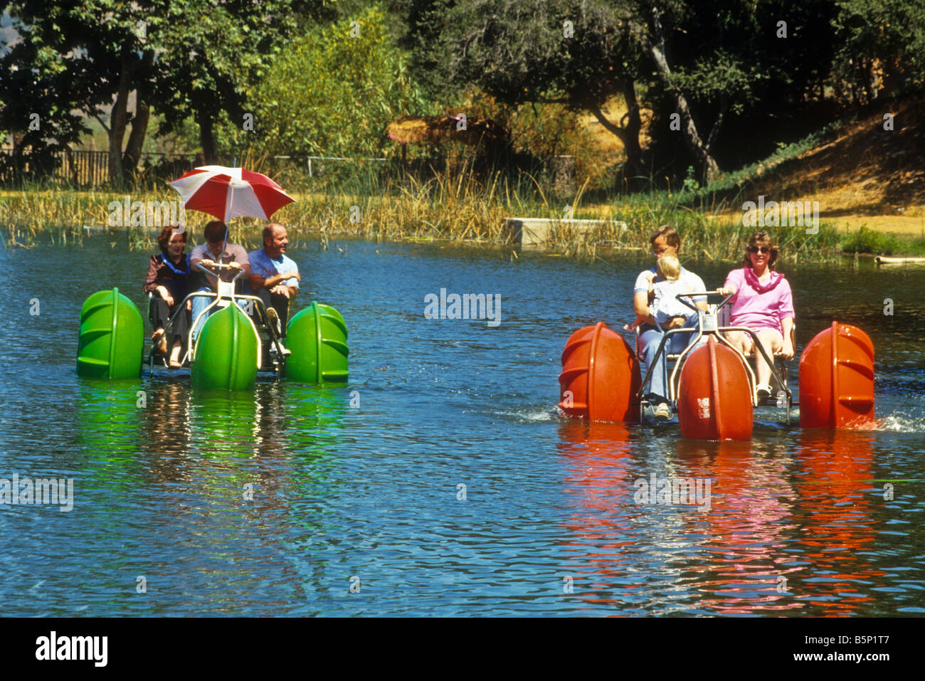 People race each other in paddle wheel boats in park lake. Stock Photo