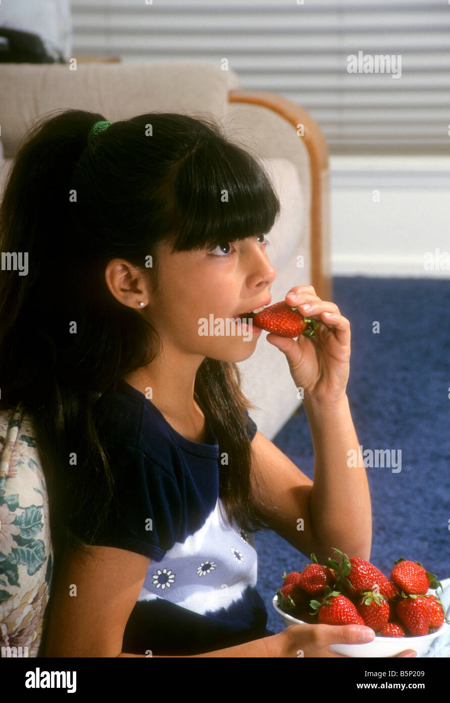 young Hispanic girl eats strawberry Stock Photo