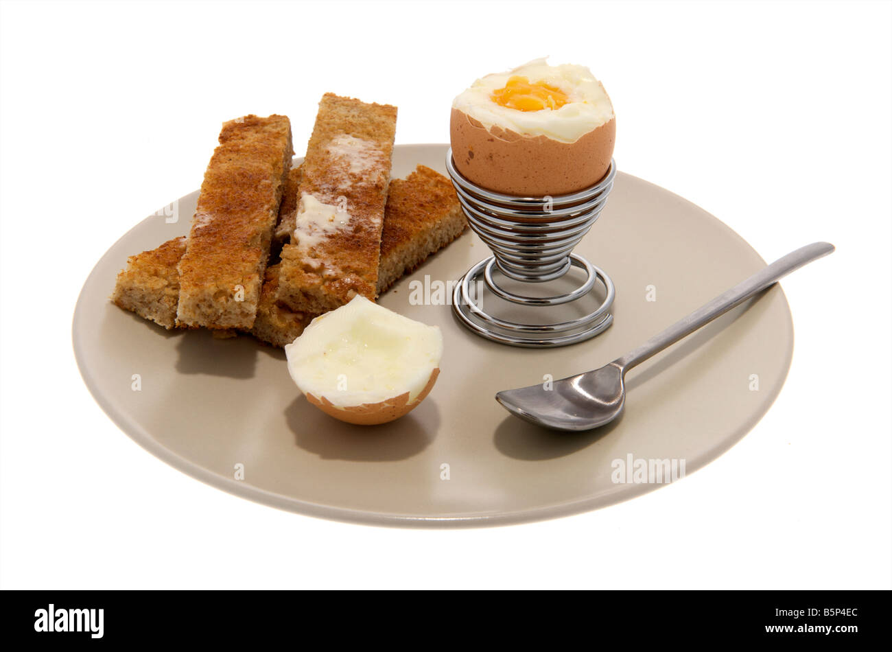 Breakfast plate of boiled egg sitting in an egg cup with the top cut off and strips of toasted bread and spoon Stock Photo