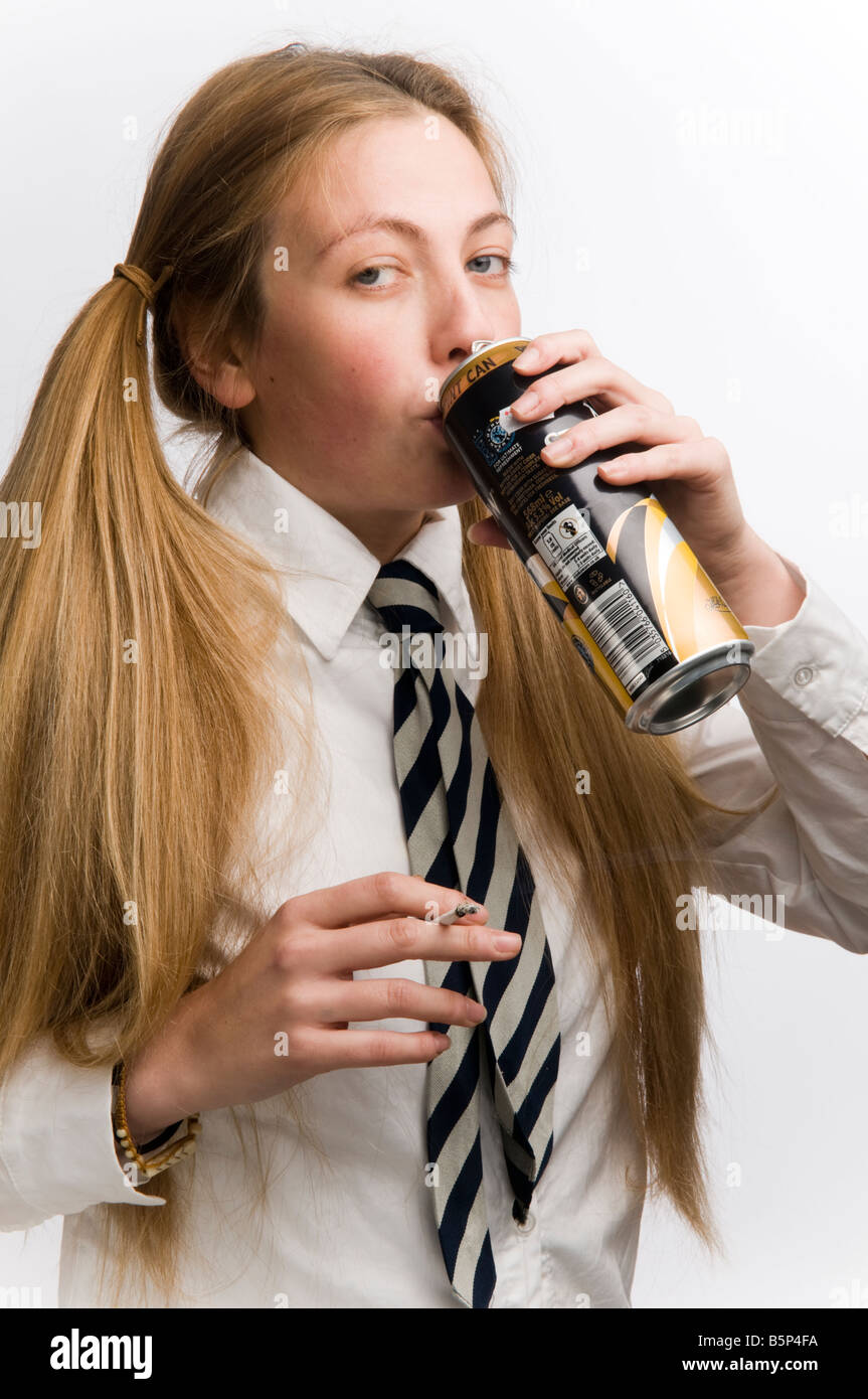 Teenage schoolgirl wearing school uniform smoking cigarette and drinking a can of cider with her blonde hair in bunches, UK Stock Photo