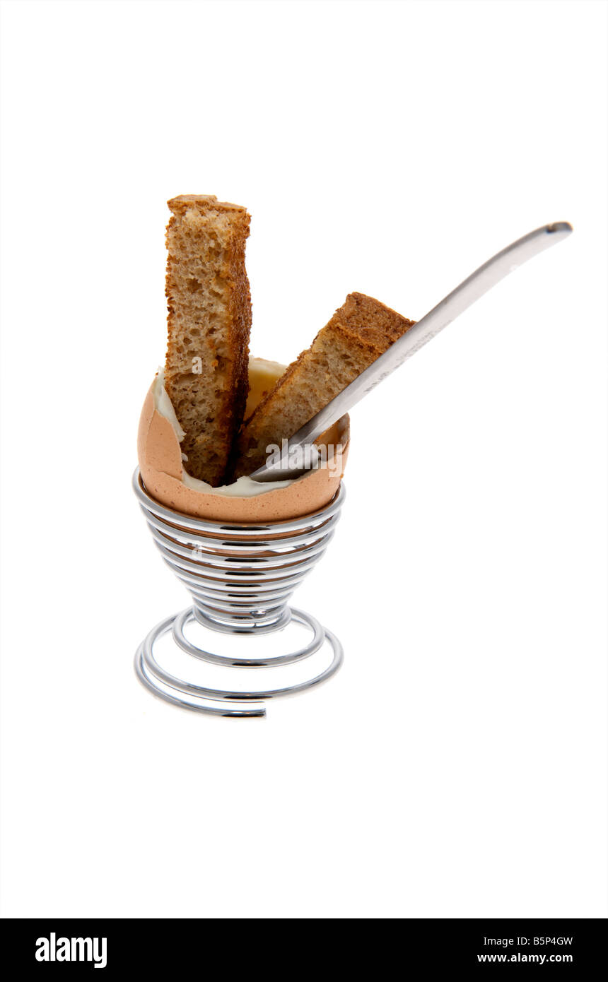 Empty Boiled egg sitting in egg cup with top cut off and a piece of toasted bread sticking out the top with teaspoon Stock Photo