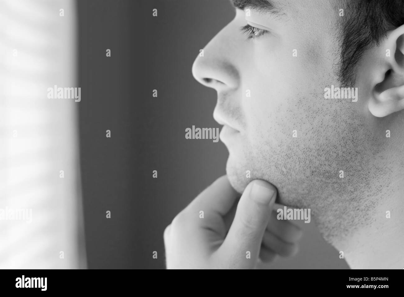 A young man with his hand on his chin thinking an important decision black and white Stock Photo
