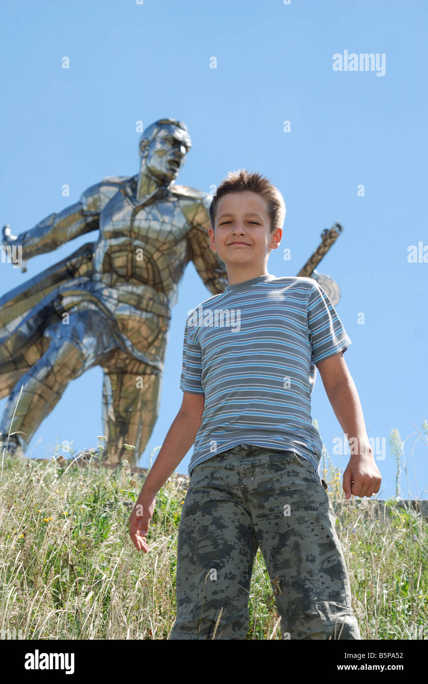 Boy stands against monument of soldier peaceful blue sky in the background sunny windy day bottom view Stock Photo