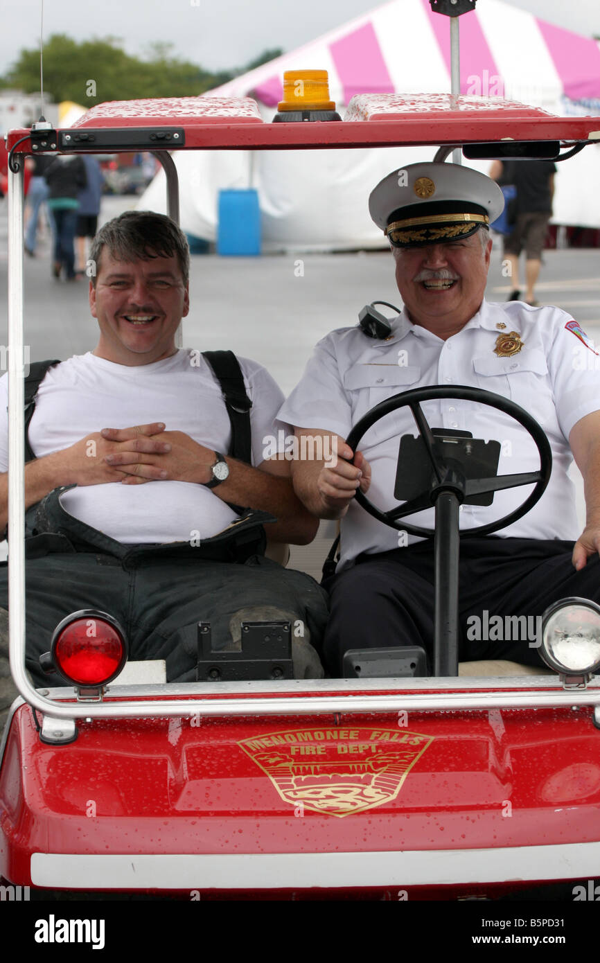 Two firefighters in a motorized cart at a fire fair enjoying themselves Stock Photo