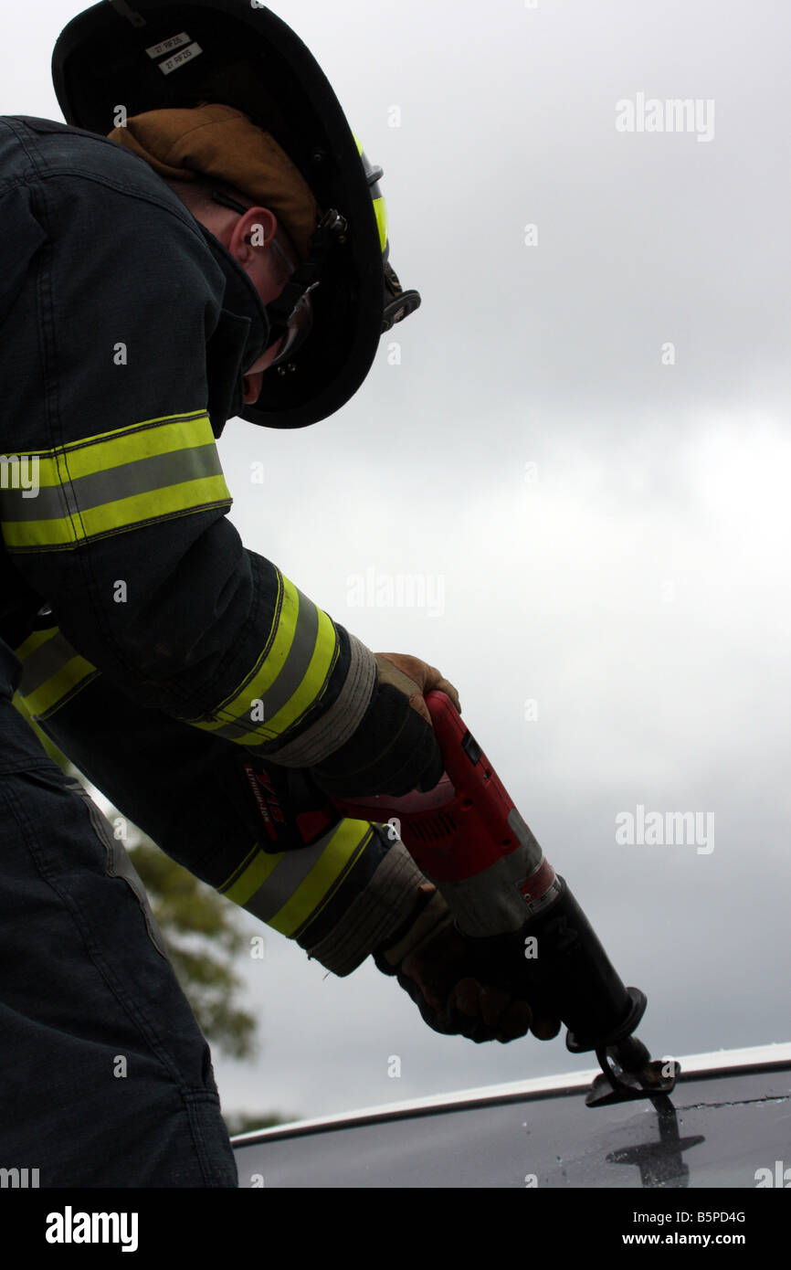 A fire fighter standing on the hood of a car to cut out the glass