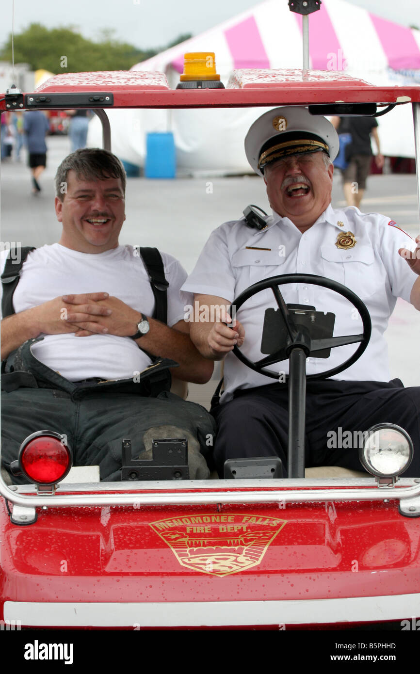 Two firefighters in a motorized cart at a fire fair enjoying themselves Stock Photo