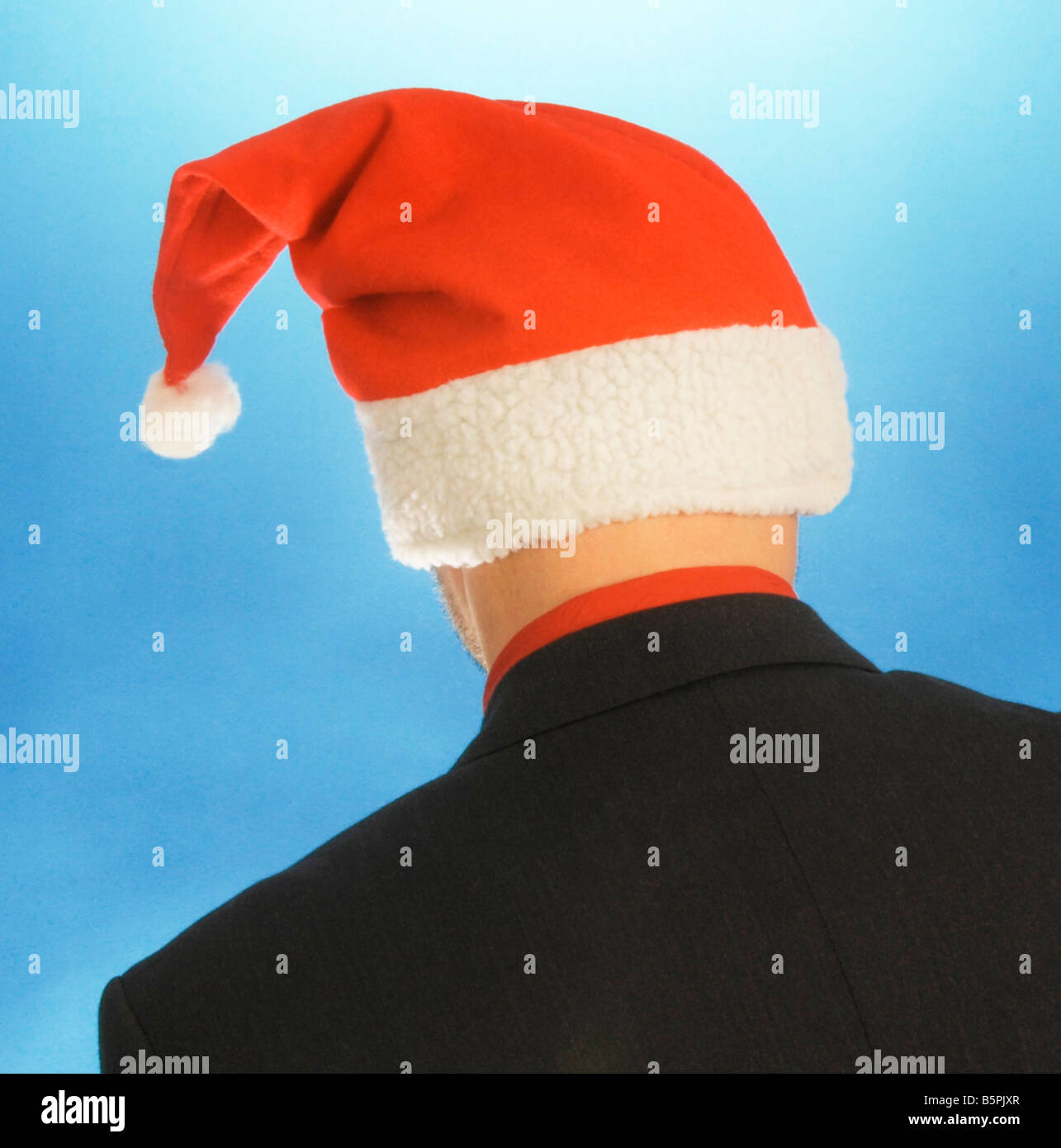 man wearing red white Santa Claus jelly bag cap hat on blue background behind back backside Stock Photo