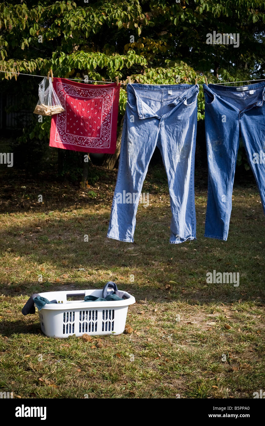 Blue jeans and a red bandanna hanging on a clothesline with a laundry basket on the ground. Stock Photo