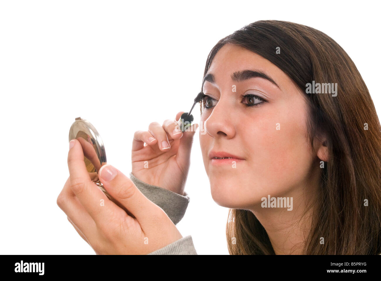 Horizontal portrait of a young girl applying mascara to her eyes in a compact mirror against a white background Stock Photo