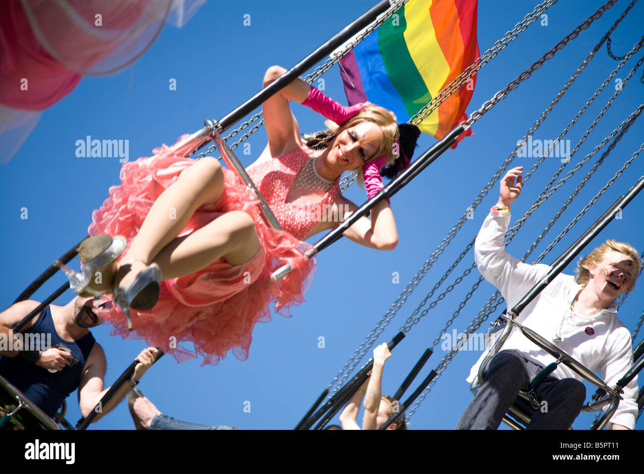 A transvestite holds on to his/her wig as she rides on the carousel at Brighton's Gay Pride fun fair. Stock Photo