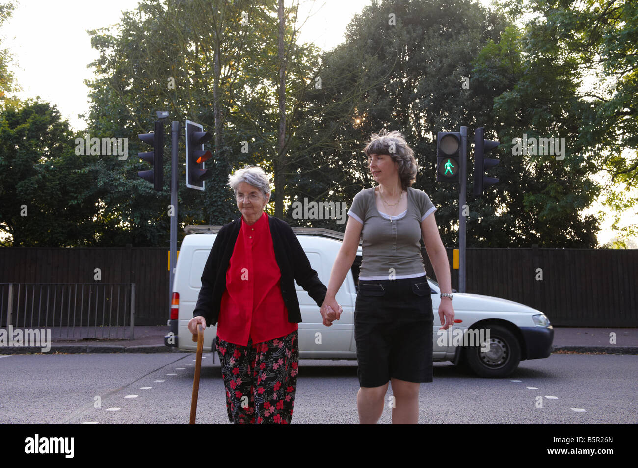 Mother and daughter crossing road using traffic lights whilst a white van hurries in a rush inpatient past over an amber light Stock Photo