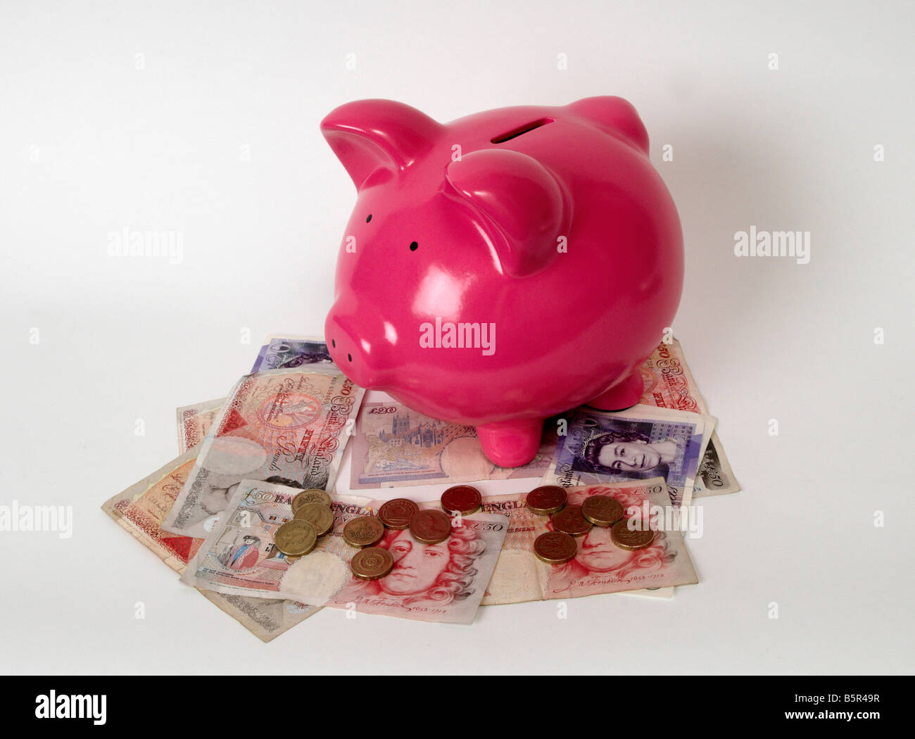 pink piggy bank sitting on a pile of british bank notes and coins Stock ...