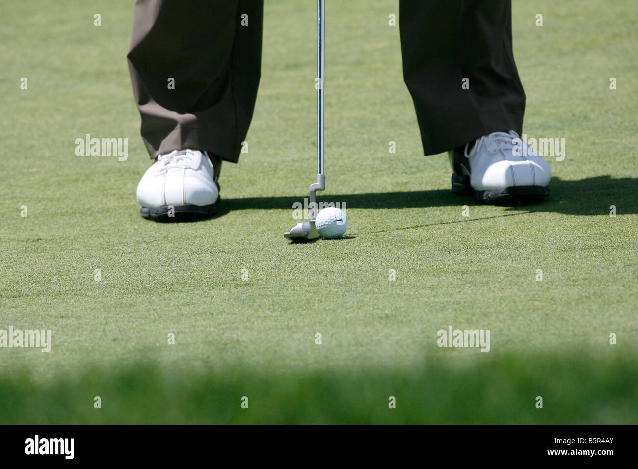 Close up of a golfer's feet, putter and ball on the putting green. Stock Photo