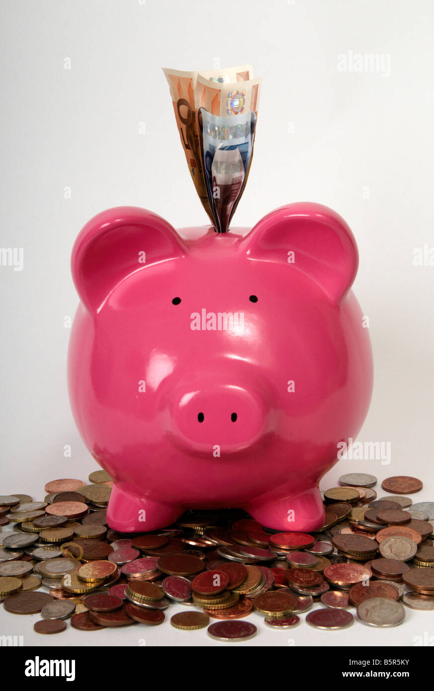 front view of a pink piggy bank sitting on a pile of coins with euro ...