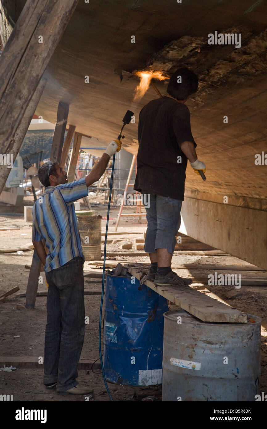 Turkish workers stripping and burning off paint from a wooden boat in a