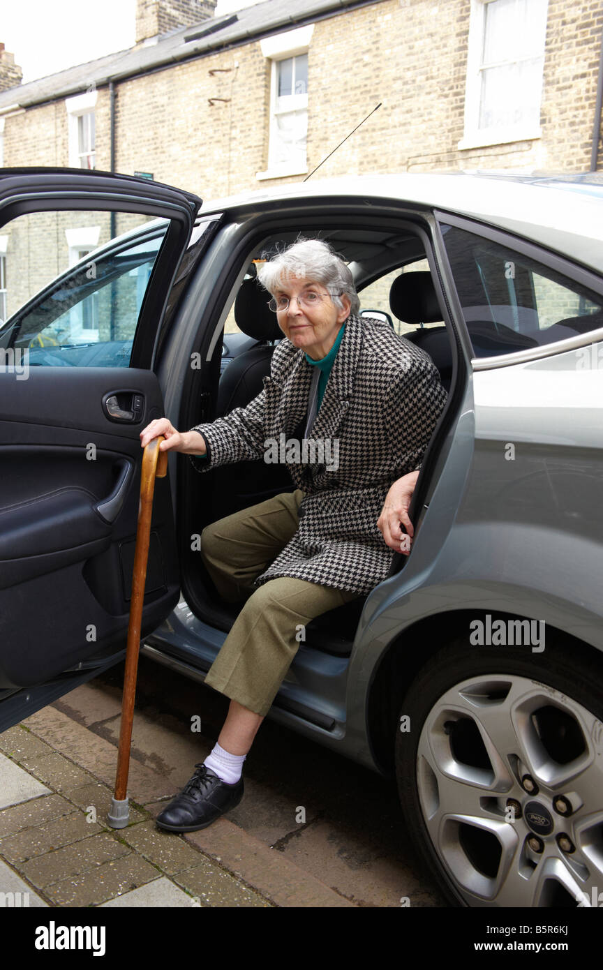 Elderly lady struggling to get out of car with walking stick Stock