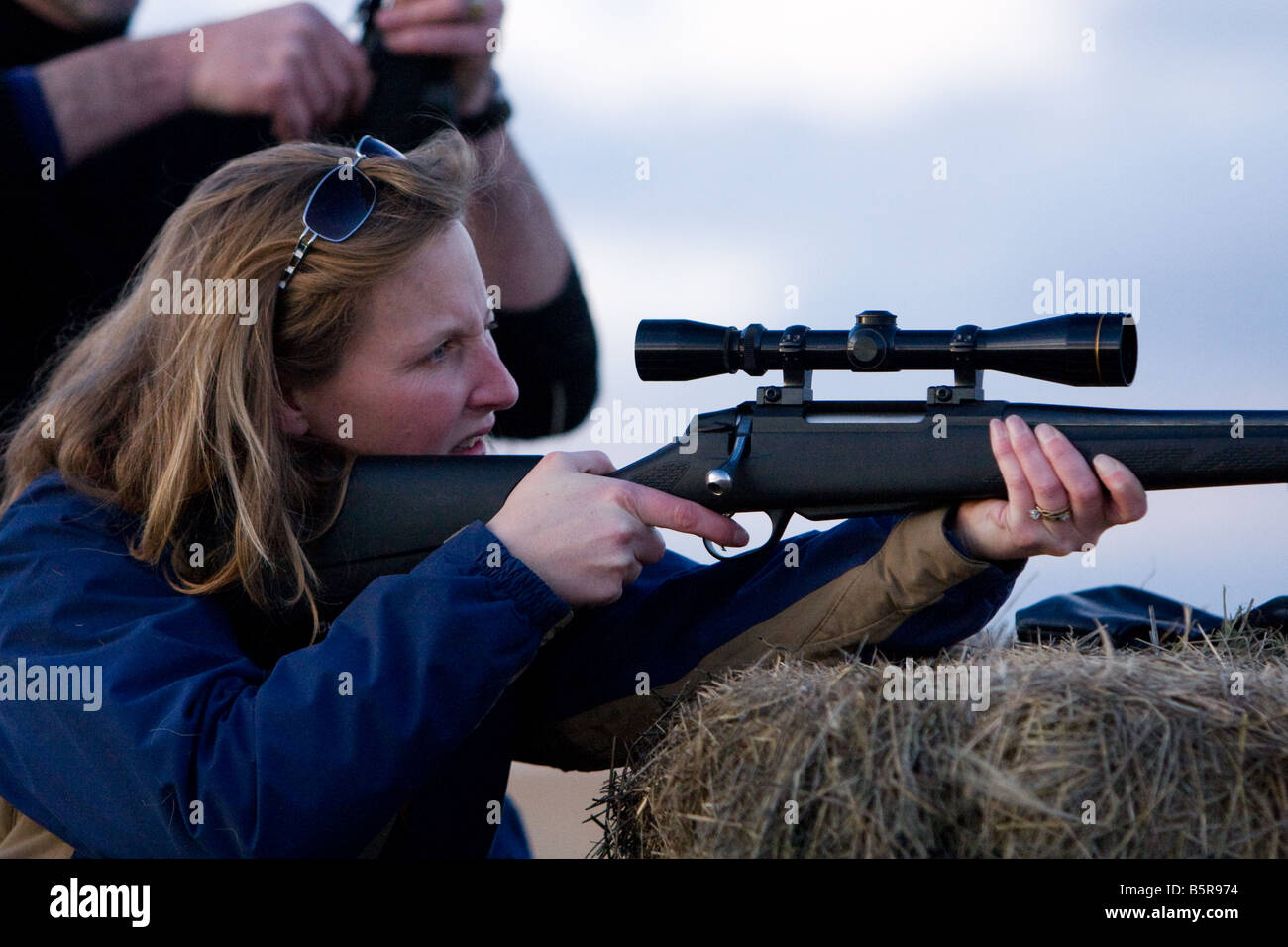 Woman shooting a rifle with scope out of the back of a truck Stock