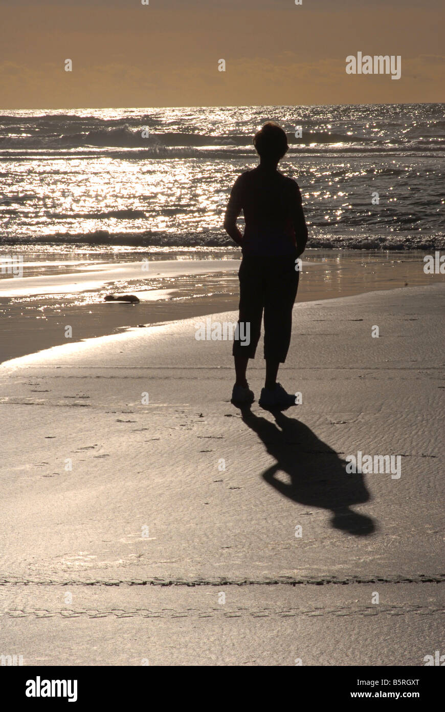 Silhouetted shape of a woman walking along a sandy shore. Grey mouth. New Zealand Stock Photo
