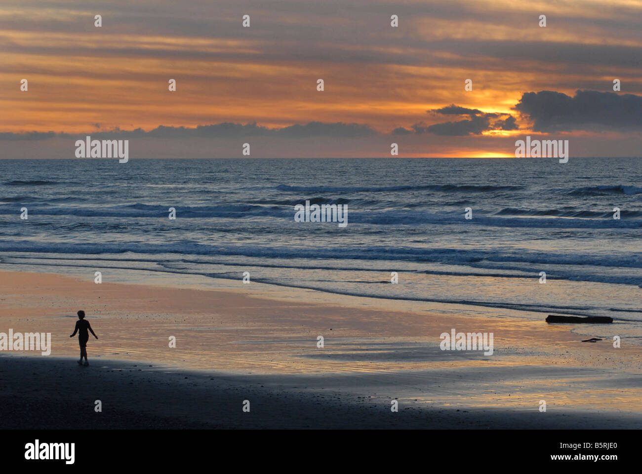 Silhouetted shape of a person a sandy shore. Grey mouth. New Zealand Stock Photo