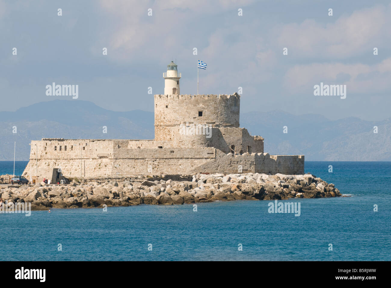St Nicholas Lighthouse in Mandraki Harbour, Rhodes, Greece, flying the Greek flag and with the coast of Turkey in the background Stock Photo