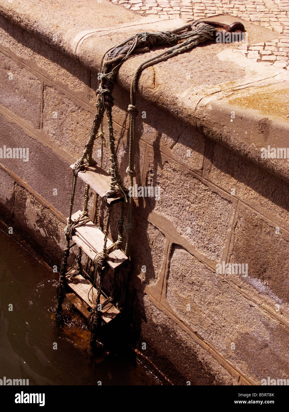 Rope ladder out of the boat, home made embarking point, harbour wall fixed to steel mooring ring, granite built landing, Stock Photo