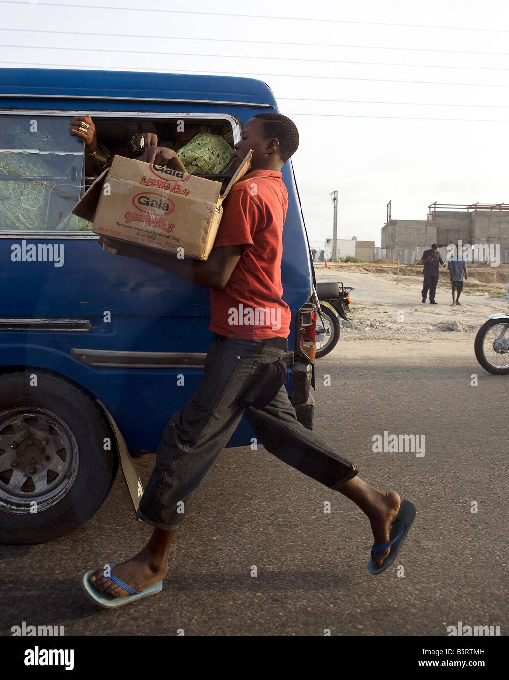 A Nigerian street seller runs alongside a local bus as he sells his produce to a traveller Stock Photo