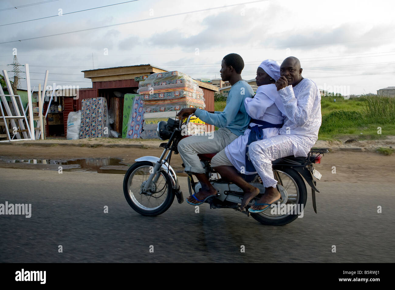 Three men share a motorbike along the road leading out of Lagos, Nigeria, on a warm sunny evening Stock Photo