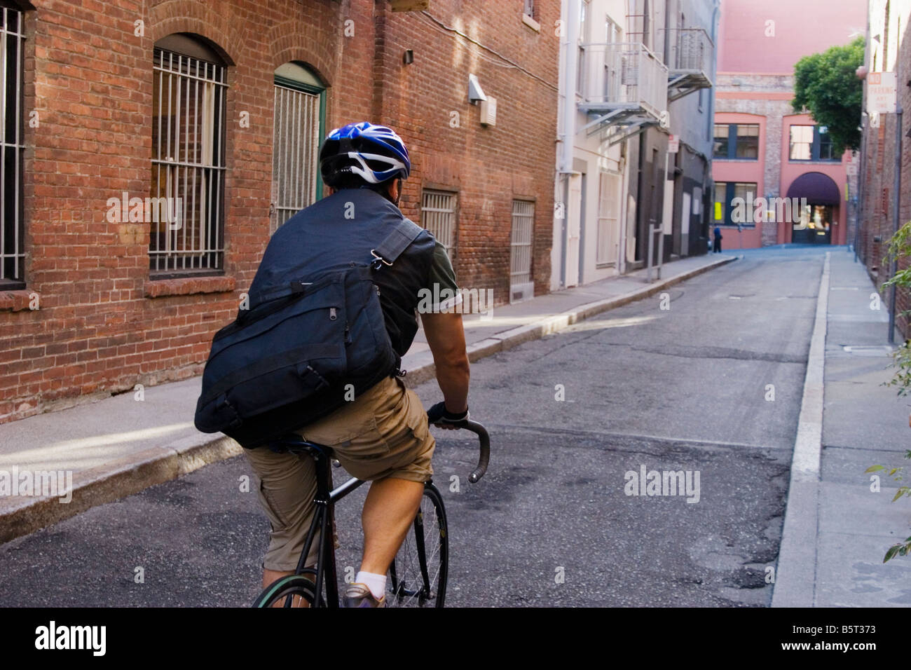 Bike messenger back view rides through an alley San Francisco California USA Stock Photo