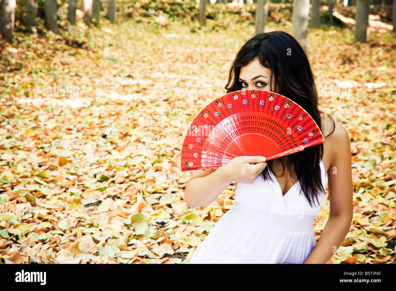Beautiful woman in a forest behind red fan Stock Photo