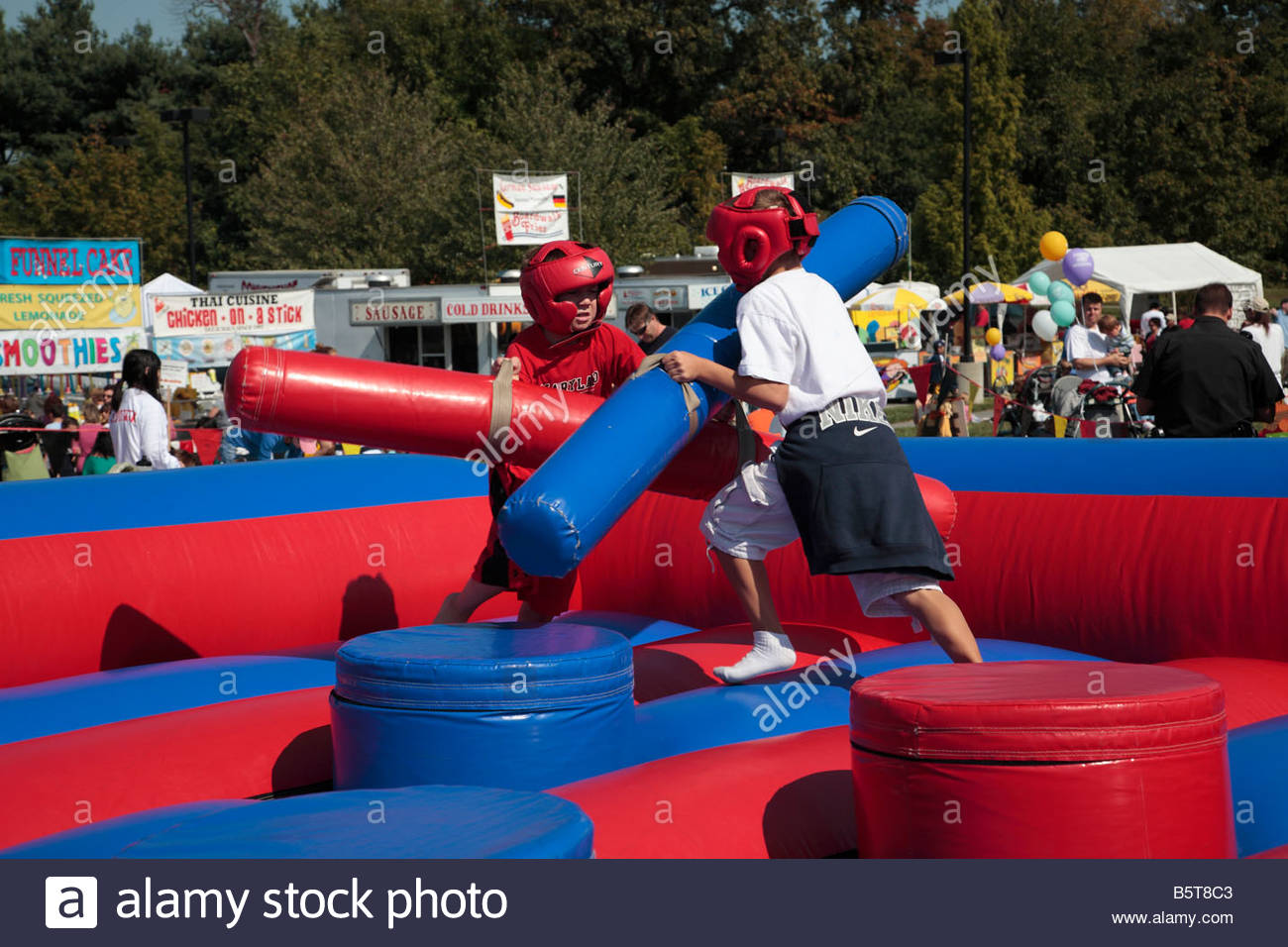 Two boys battle with foam pugil sticks at an Octoberfest carnival Stock