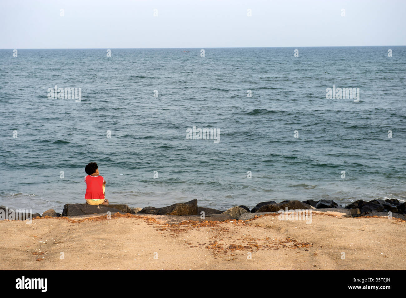 Child sitting on the waterfront in Pondicherry India. Stock Photo
