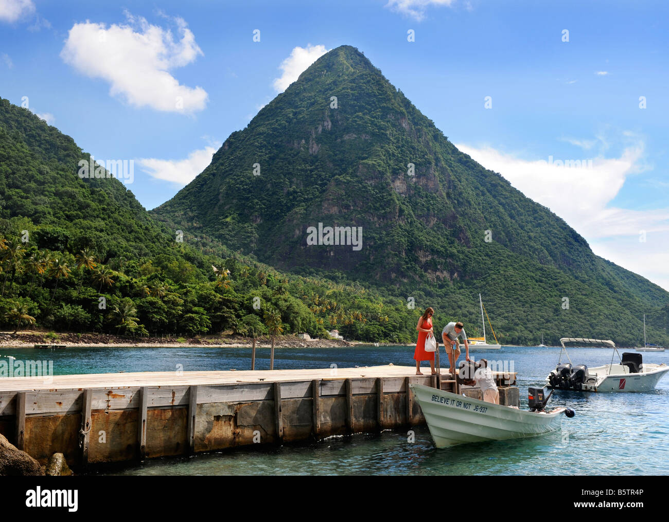 A TOURIST COUPLE LOAD THEIR SUITCASES ONTO A WATER TAXI FROM A JETTY OFF FORBIDDEN BEACH AT THE JALOUSIE PLANTATION RESORT ST LU Stock Photo