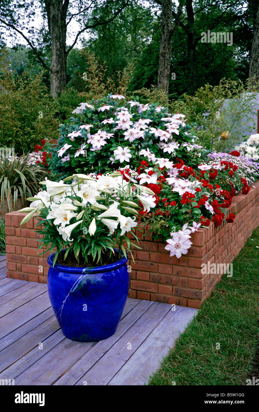 A colourful raised flower bed with container of Lillies Stock Photo