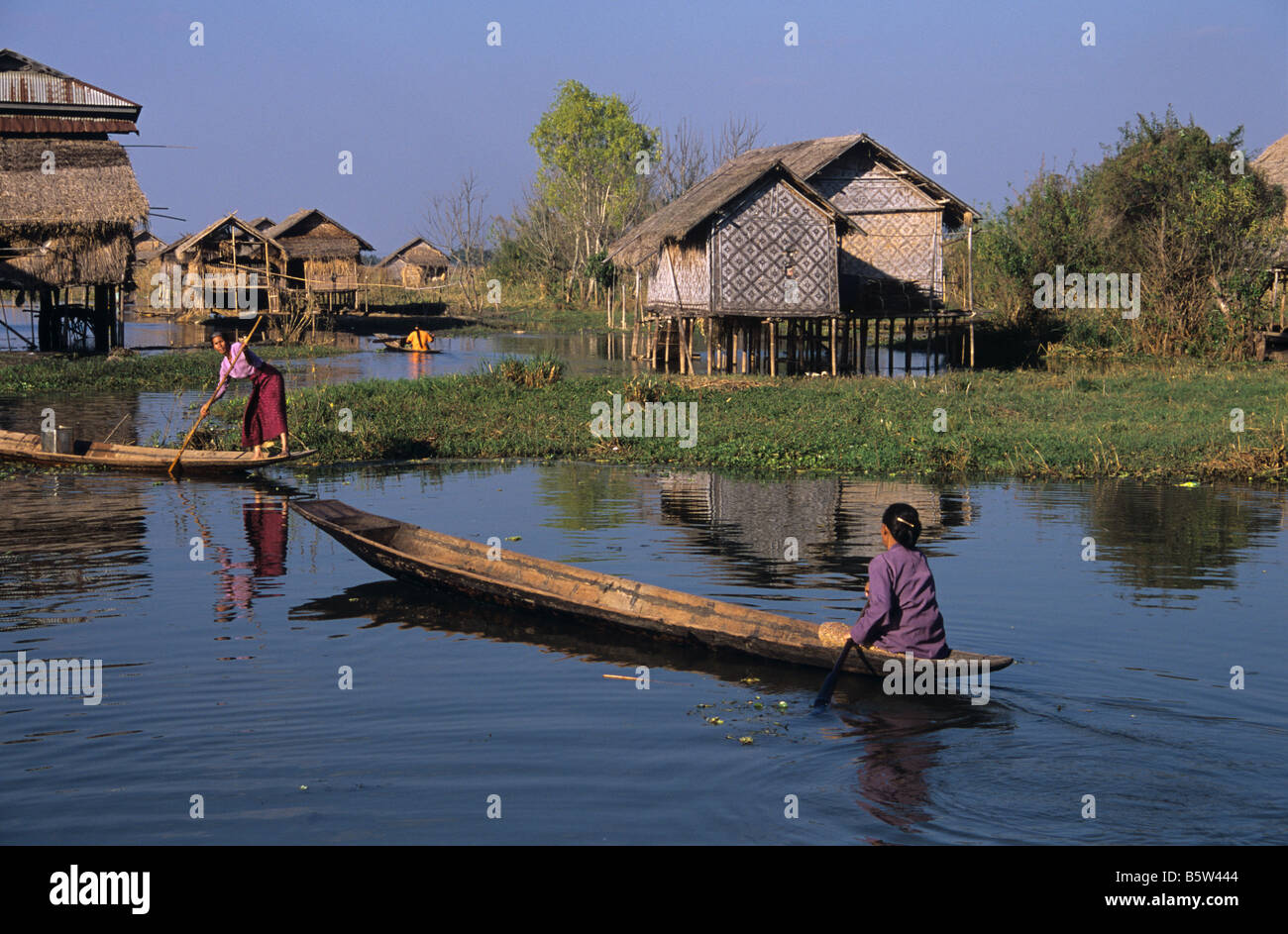 Burmese women canoe through a stilt village raised up on pilotis, Inle