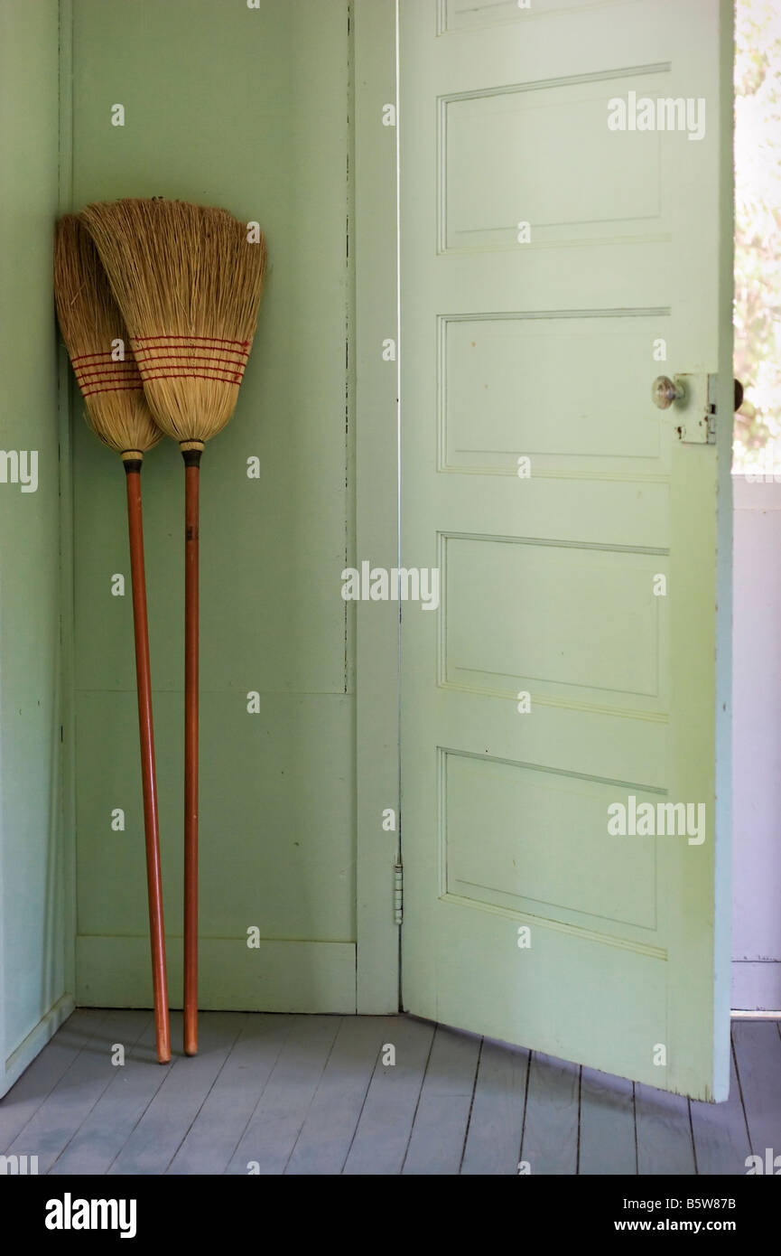 Cleaning brooms propped up in the corner of a pastel green door entrance to a pastel green room Stock Photo