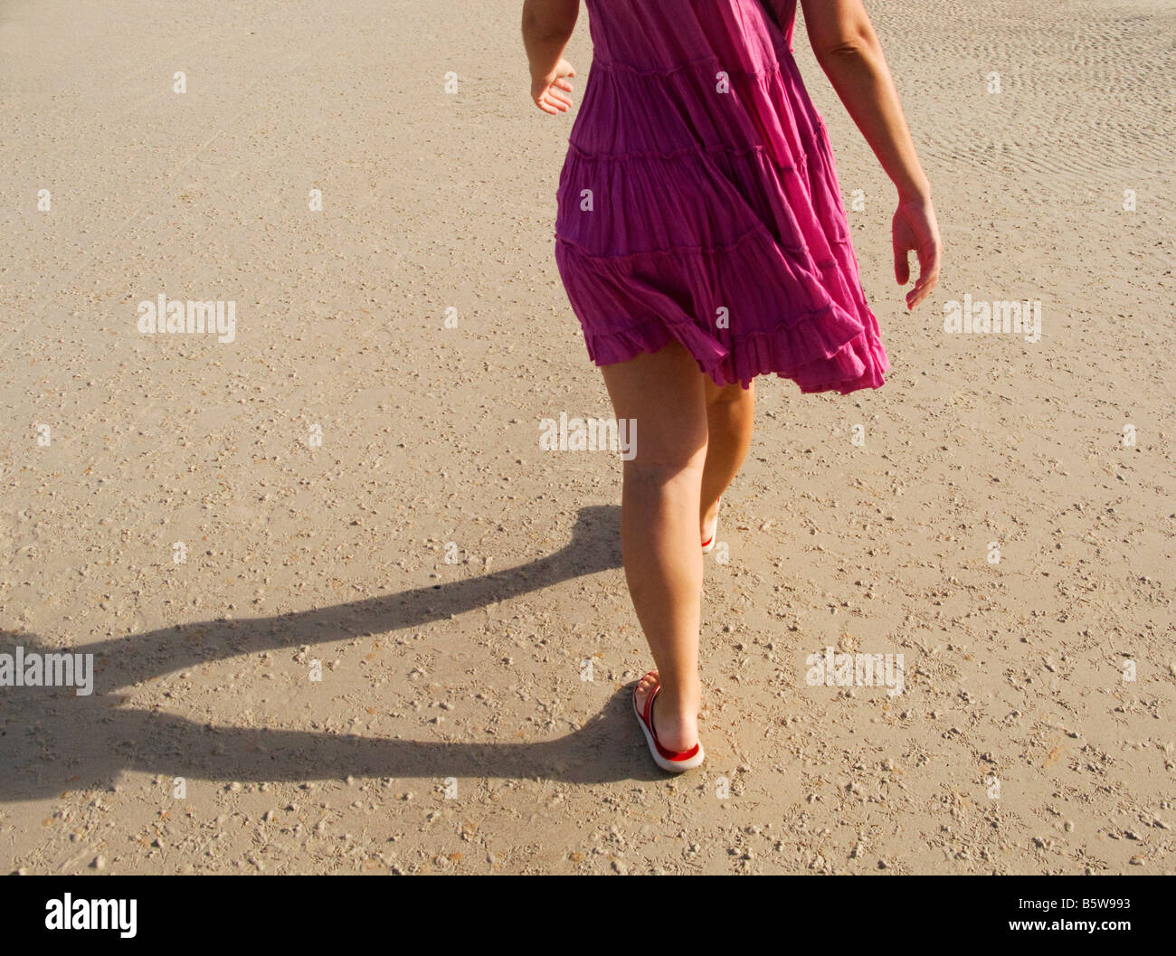 Woman in pink dress walking along the beach Stock Photo - Alamy