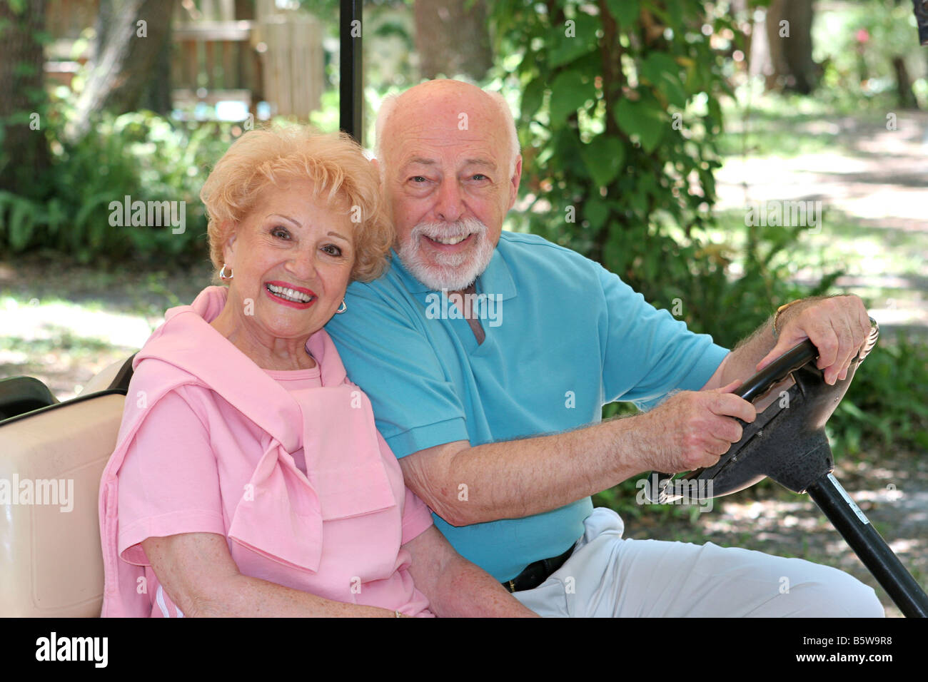 A happy senior couple driving a golf cart through a resort Stock Photo