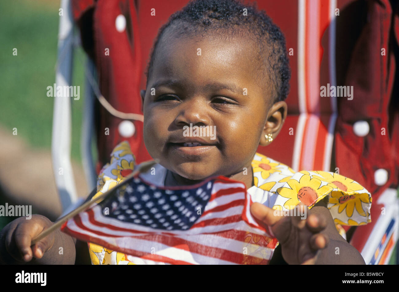 A cute little african american girl watches a 4th of july Fourth Of July July 4th parade while waving an American flag, St. Louis, Missouri. Stock Photo