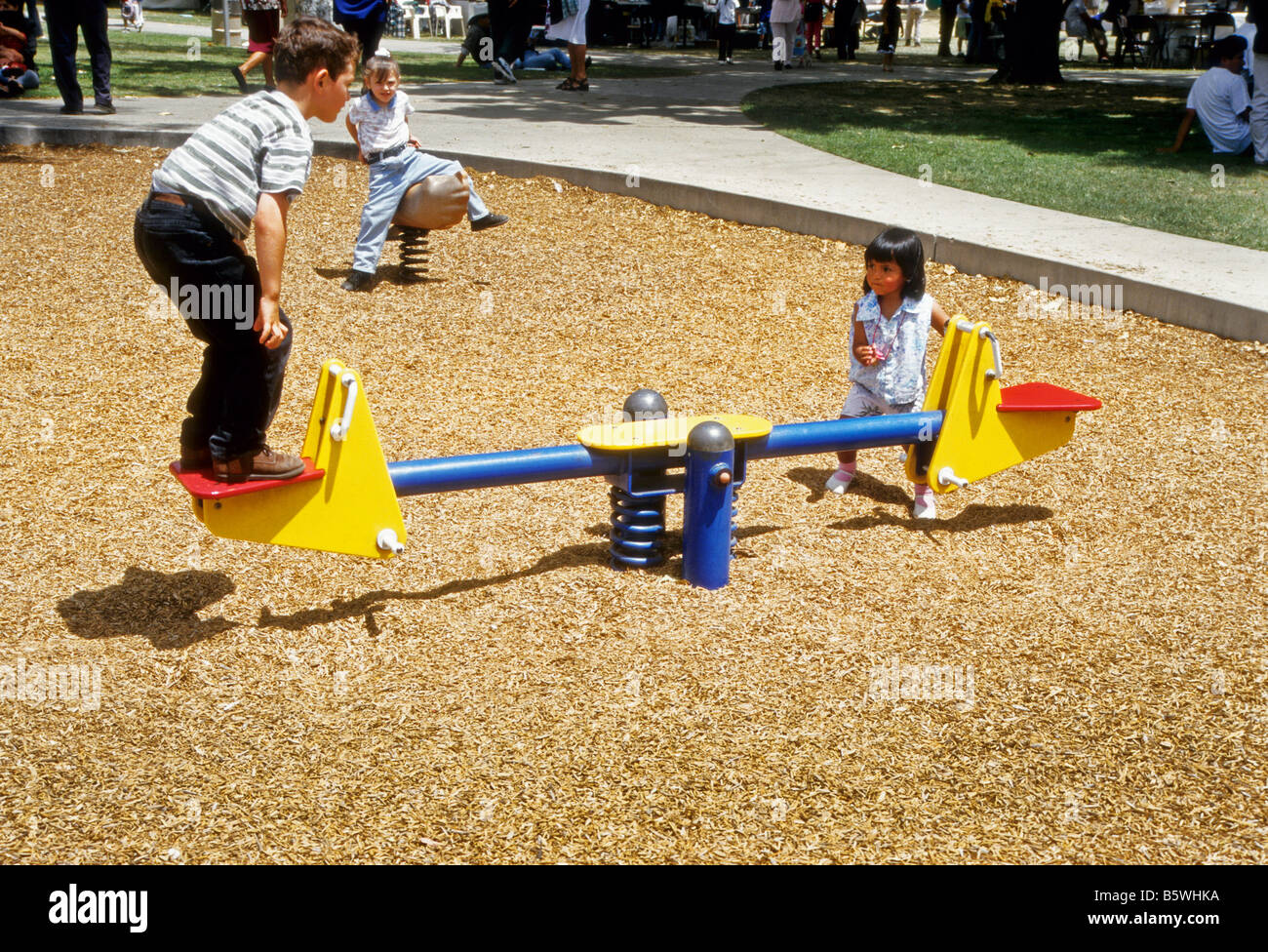Children play on safety version of teeter-totter in park playground Stock Photo