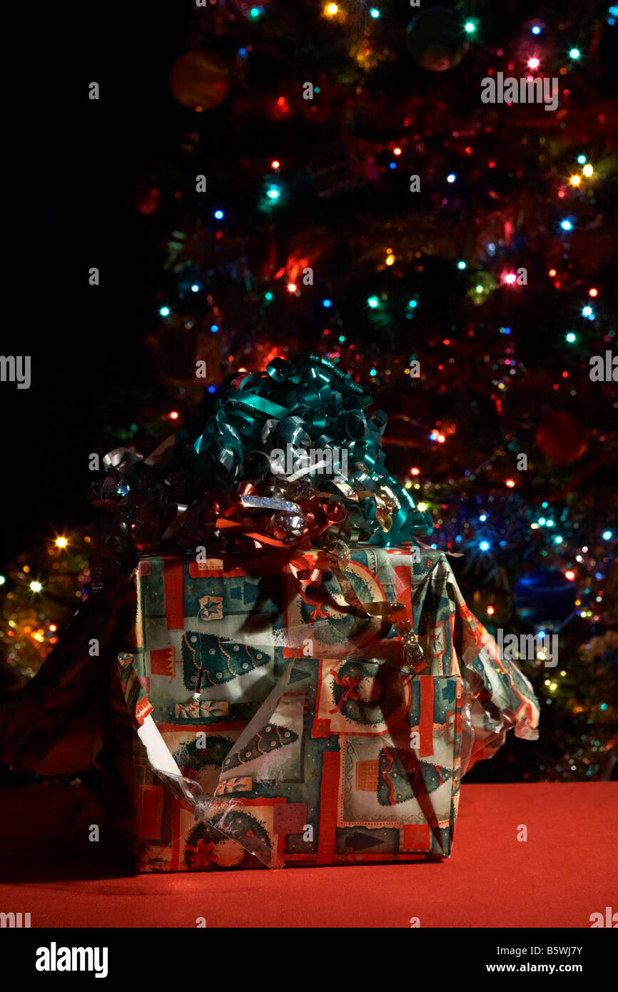 badly wrapped partially opened christmas present in front of christmas tree Stock Photo