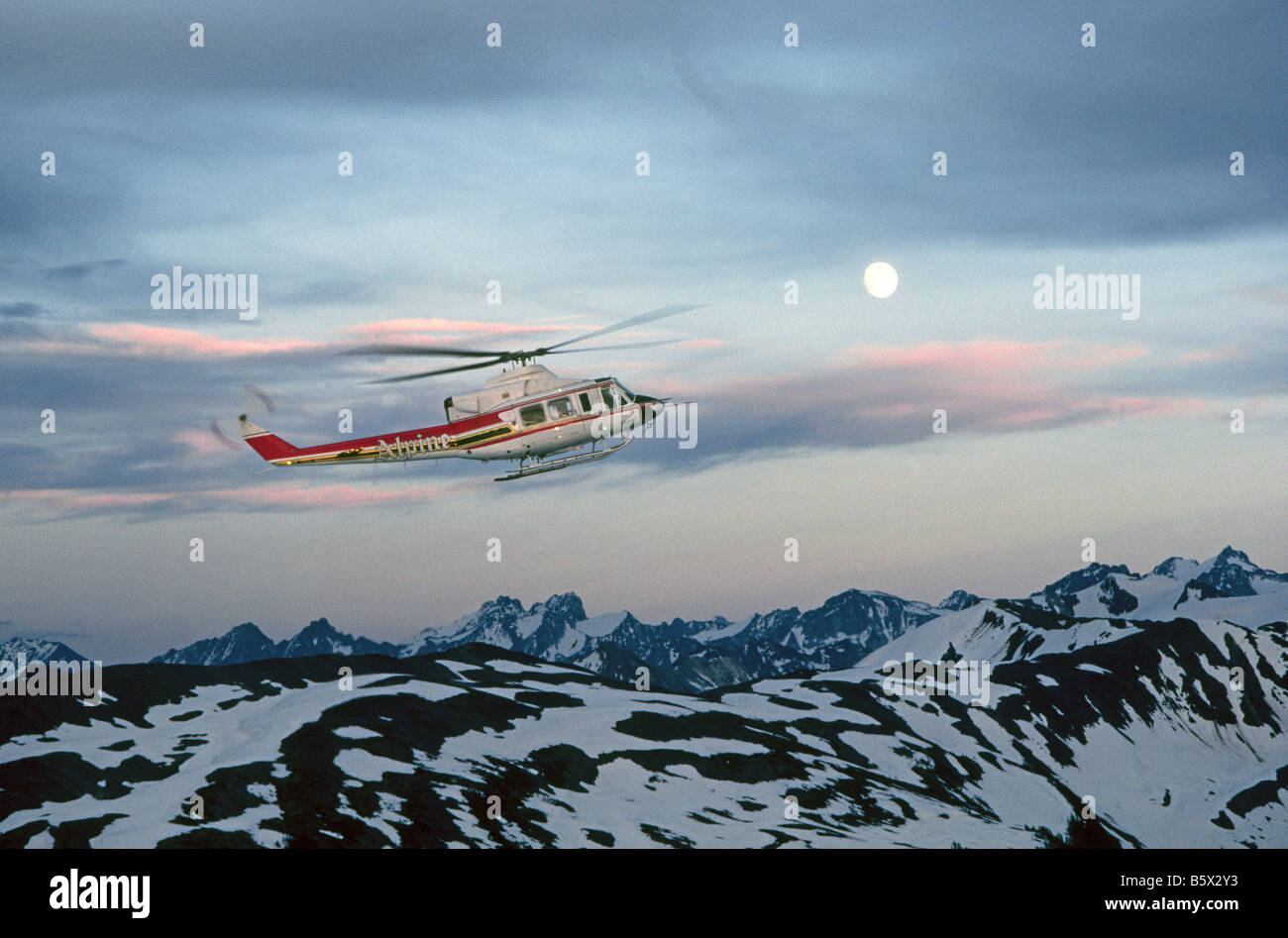 A Canadian helicopter carries hikers out of the Rocky Mountains just before dark as the moon rises in Banff National Park, Alberta, Canada. Stock Photo