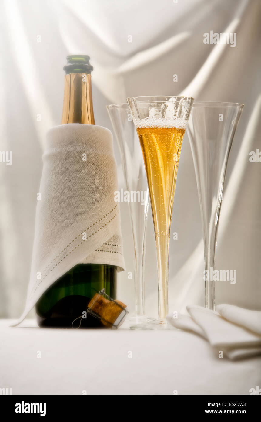 two champagne glasses with a champagne bottle on a white fabric draped