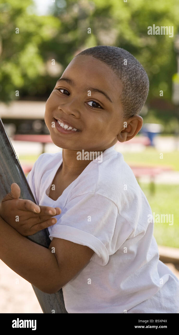 A smiling Afro-American 4 year old male child  is playing at a public playground on a beautiful summer day. Stock Photo