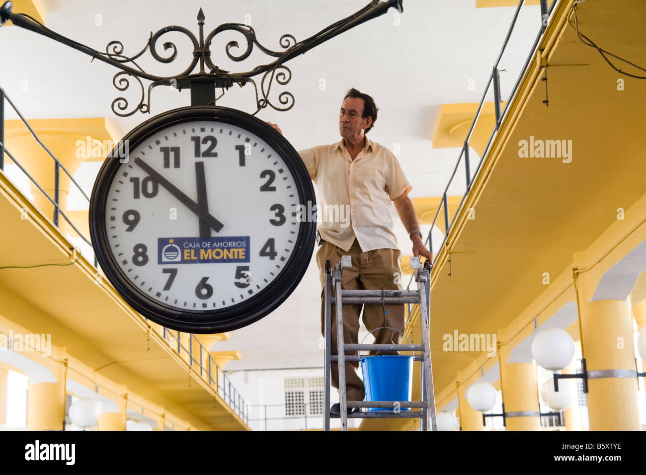A man standing on a ladder cleans the giant clock hanging in the bus