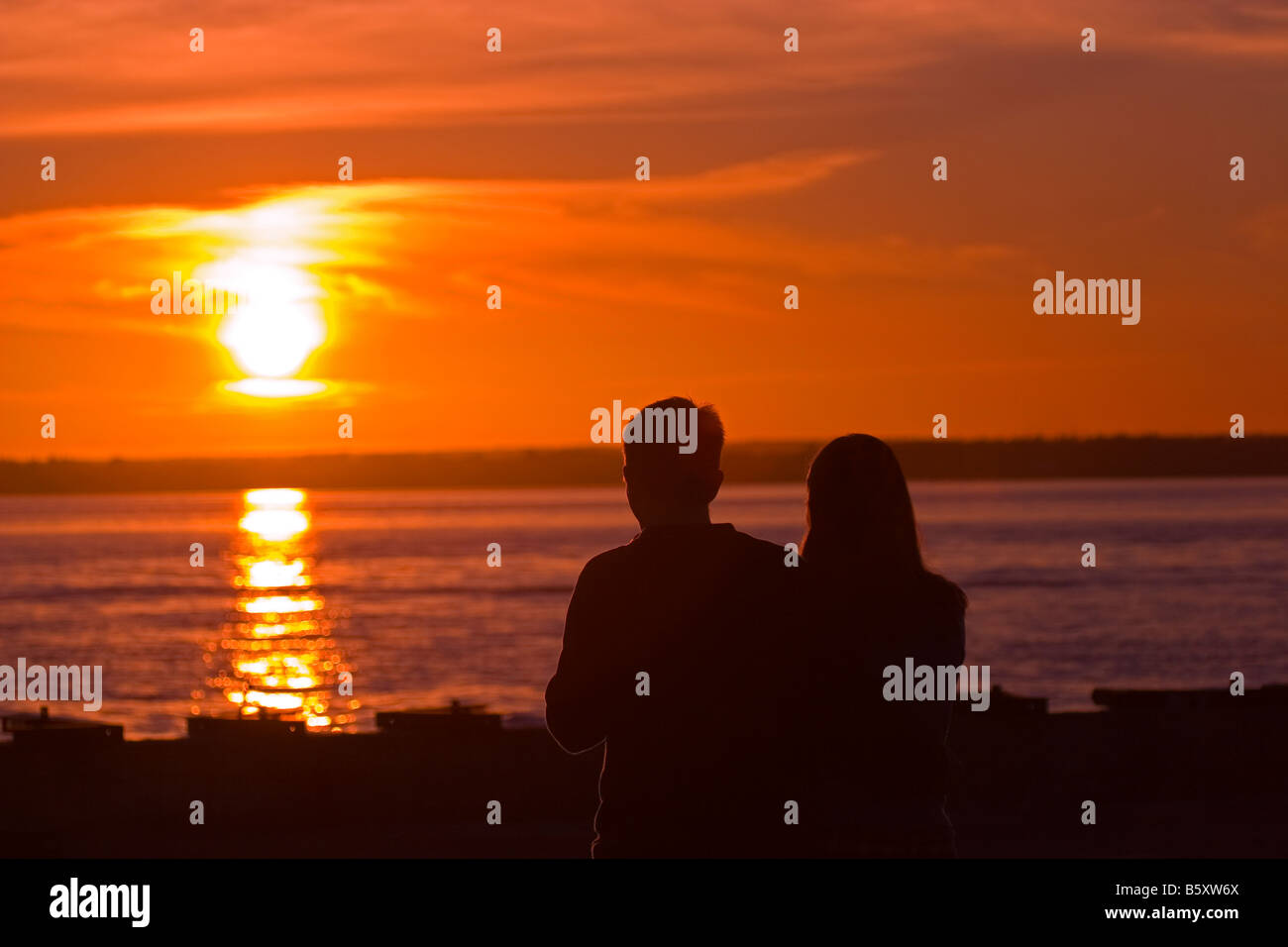 Silhouette of young couple standing on beach at sunset Stock Photo - Alamy