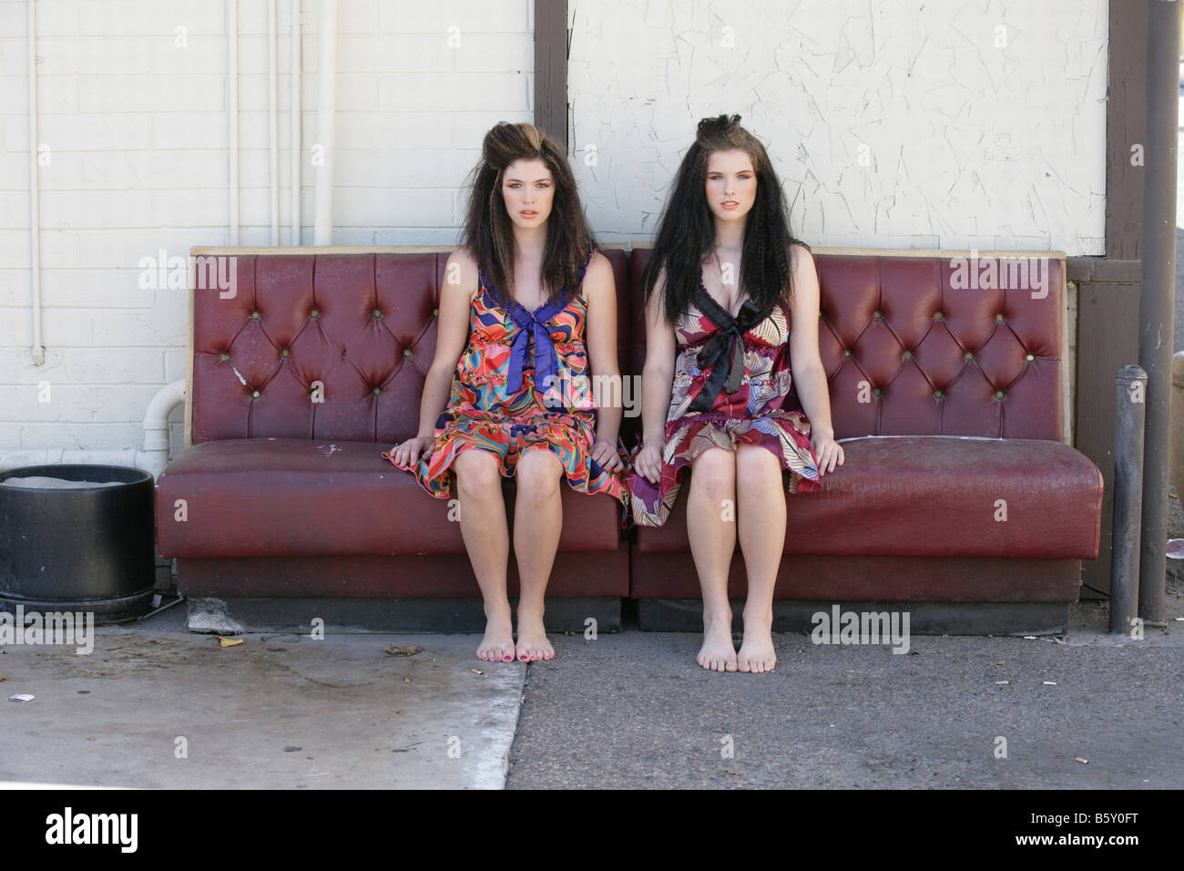 two sisters share a leather couch in patterned dresses Stock Photo